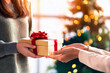 © Medical Works - Hand of woman offer gift box to lovers on christmas tree light background. have a copy space for text. Close up on woman hands giving Christmas present. Christmas gift.