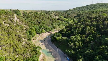 Poster - Drone footage over a rural road under dense forest trees and green hills on a sunny day