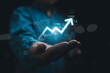 © Dilok - Businessman holding glowing increasing up arrow with stock market graph chart and world map for global economic growth concept.