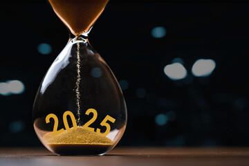 Wall Mural - hourglass with 2025 on dark background with bokeh and copy space for preparation and countdown of ne