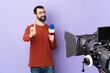 © luismolinero - Reporter man holding a microphone and reporting news over isolated purple background showing and lifting a finger