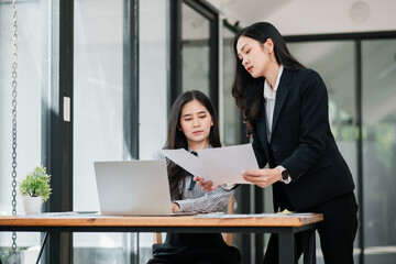 Wall Mural - Two businesswomen discussing documents in a modern office, showcasing teamwork and collaboration.