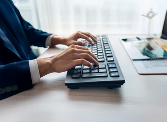 Aufkleber - Close-up of hands typing on a dark keyboard at a desk.  The person is wearing a suit jacket. The setting appears to be a modern office.