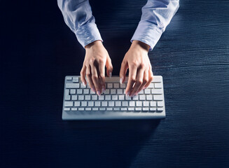 Aufkleber - Overhead shot of hands typing on a white keyboard on a dark wooden desk.  The scene is dimly lit, suggesting nighttime work.