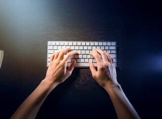 Aufkleber - Overhead view of hands typing on a wireless keyboard at night, illuminated by soft light.  A mouse is partially visible.