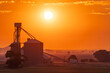 © Austockphoto - Distant view of a glowing sun in a golden sky over a grain silo