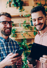 Wall Mural - cheerful hipster guys laughing together share funny common photos via bluetooth connection, carefree