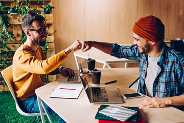prosperous male it developers clinking fists in sign of agrement cooperating on common startup proje
