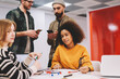 © BullRun - Portrait of african american female designer smiling at camera while working together with colleagues on new building project in office studio.Male and female students collaborating in university