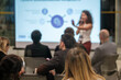 © Anton Gvozdikov - Audience attentively listens to female speaker during business presentation in modern conference setting. Engaged participants focus on screen content.
