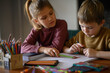 © Mariia Andreeva - A kids sit at a table, joyfully drawing New Year’s themed pictures. Surrounded by a colorful array of pencils, markers, and pens, they embrace the festive spirit with their creative