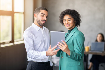 Leinwandbilder - Two professionals engage in discussion while sharing a tablet in a contemporary office environment. The atmosphere reflects teamwork and diverse perspectives, fostering collaboration.