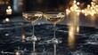 © Alienmarsh - Two champagne coupes on a dark marble table with bokeh lights in the background.