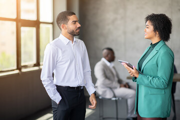 Leinwandbilder - Two professionals are talking in a bright office space, showcasing teamwork and diversity. Others are seated in the background, highlighting collaboration in a corporate environment.