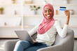 © Prostock-studio - Easy Payments. Portrait Of Smiling Black Muslim Woman In Hijab With Laptop And Credit Card Posing In Home Interior, Happy African Islamic Lady Shopping Online While Sitting In Comfortable Chair