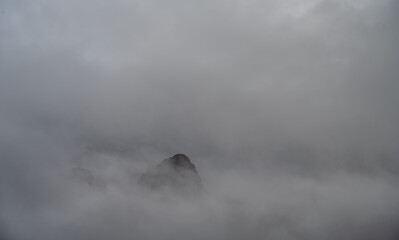 Wall Mural - an isolated rocky mountain peak showing through thick clouds and fog