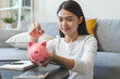 © KMPZZZ - Saving money wealth concept, asian young business woman hand putting coin into piggy for saving cost, cash finance planning to spend enough money on her income for save money, payment tax, investing.
