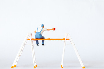 Wall Mural - Miniature figure of a painter sitting on ladders holding a red paint can on white background