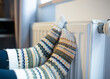 © Yuliya - Woman with her feet resting on a radiator to warm them up by the cold of winter and energy saving.