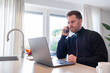 © ReLein - working at home in the kitchen. caucasian male sitting at the kitchen counter behind his laptop working and communicating.