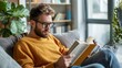 © iuricazac - A man is engrossed in reading a book sitting comfortably On a gray couch in a cozy living room.