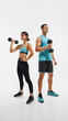 © master1305 - Full-length image of young woman and man with fit, sportive,strong bodies, standing with dumbbell in hand, posing against white studio background. Sport, active and healthy lifestyle, workout concept
