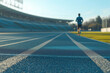 © Danica - The image captures a runner jogging on a blue track in an outdoor stadium under clear daylight, emphasizing focus and determination