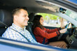 © AntonioDiaz - Smiling father teaching his teenage daughter to drive inside a car, both wearing seatbelts