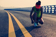 © lzf - Fitness woman runner tying shoelace on seaside bridge