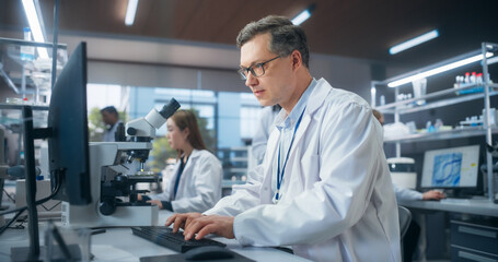 Leinwandbilder - Handsome Adult Scientist Wearing Glasses and a White Lab Coat, Studying DNA Samples and Evaluating Data on Computer. Group of Multiethnic Specialists Working in a Laboratory