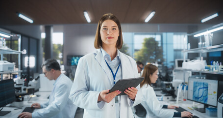 Aufkleber - Portrait of a Beautiful Caucasian Lab Engineer in White Coat Looking at Camera and Smiling. Genetic Research Scientist Holding Tablet Computer in a Busy Applied Science Laboratory