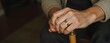 © chaiyadid - A weathered hand, adorned with a golden band, rests gently on a cane; a poignant image of age and resilience.