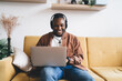 © BullRun - Cheerful dark skinned male freelancer in headphones using laptop application for browsing website in home interior, happy African American man in electronic device searching music podcast on netbook