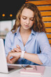 © BullRun - Serious female freelancer checking time on electronic smartwatch while waiting for meeting with colleague in cafeteria, young woman tracking gps via wristwatch during distance job in coworking space