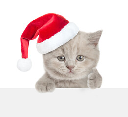 Aufkleber - Cute tiny kitten wearing red santa hat looking above blank white banner and showing thumbs up gesture. isolated on white background
