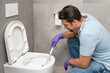 © Vitaliy - Сlose-up shot of a frustrated man cleaning a toilet using a special cleaning product and a brush