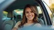© Viktor_D - woman sits in the driver's seat of her car, smiling and looking at the camera while taking a selfie with her cell phone