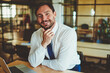 © BullRun - Portrait of cheerful male economist in formal wear sitting at desktop with laptop device and smartphone and looking at camera, successful man employee spending time in office and waiting colleague