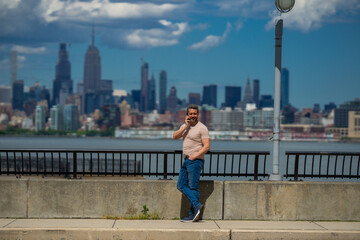 Wall Mural - Man talking at the phone in New York City. Man talking on the phone on NY skyline. Man in t-shirt talking on cell phone. Guy talking by mobile phone. Tourist in city street holding smartphone.