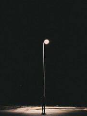 Poster - A solitary person stands quietly beneath a streetlight on an empty street at night, surrounded by darkness and casting long shadows. Generative AI