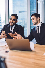 Wall Mural - Happy multicultural male colleagues smiling during brainstorming meeting using smartphone device for browsing website for networking, cheerful business consultants enjoying friendship at job