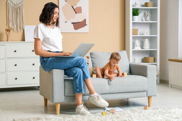 Poster - Cute little baby and happy young mother working with laptop on maternity leave at home