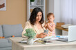 © Pixel-Shot - Cute little baby and young mother working with laptop while using mobile phone on maternity leave at home