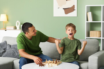 Canvas Print - Happy father with his little son playing chess together on sofa at home