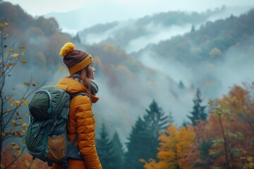 Wall Mural - A woman looks out from a foggy forest, wearing a yellow jacket and backpack