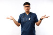 © ArvStd - Healthcare workers concept. Troubled and confused asian male nurse in scrubs and medical asking question, shrugging and look concerned, white background