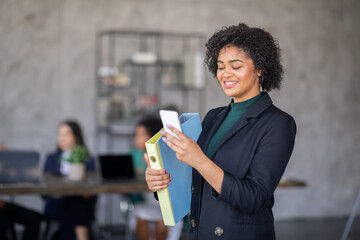 Leinwandbilder - A diverse group of professionals engages in productive teamwork at a modern office. One woman checks her phone while holding folders, highlighting effective communication and collaboration.