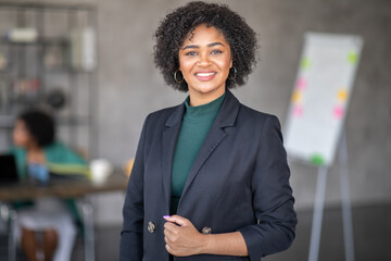 Leinwandbilder - A professional woman stands confidently in a contemporary office, showcasing teamwork and cooperation. Colleagues engage in productive discussions, thriving in a dynamic corporate environment.
