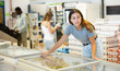 © JackF - Young woman standing at display refrigerator and choosing frozen food. Girl shopping in supermarket.