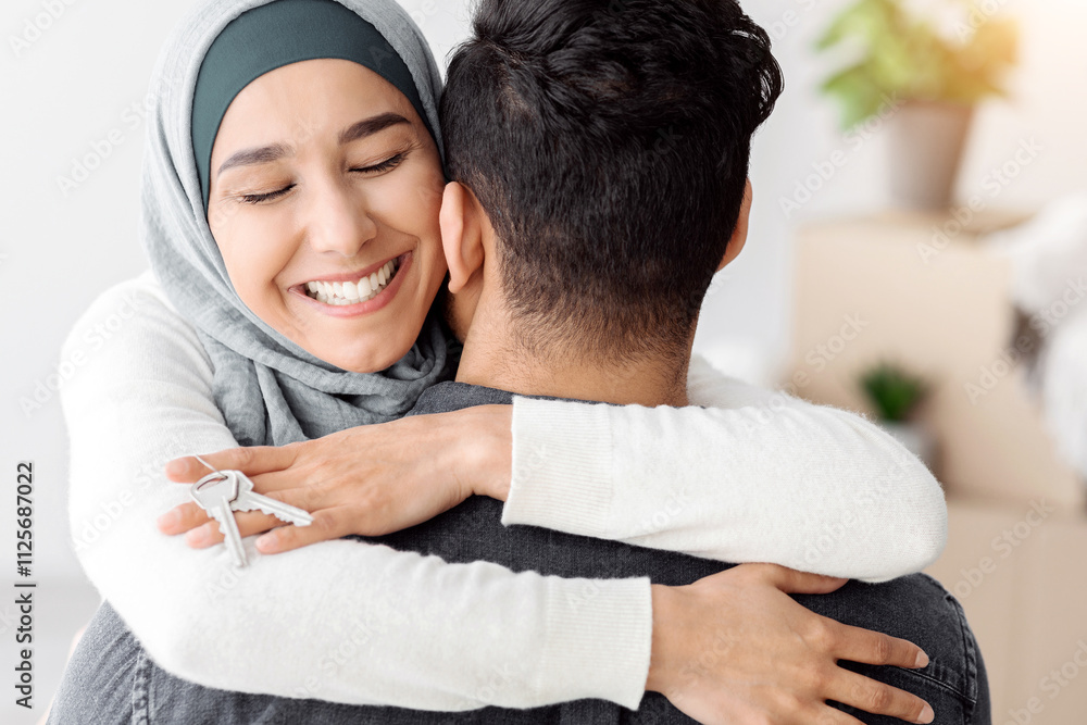 Happy young lady in hijab with keychain hugging her husband and smiling ...